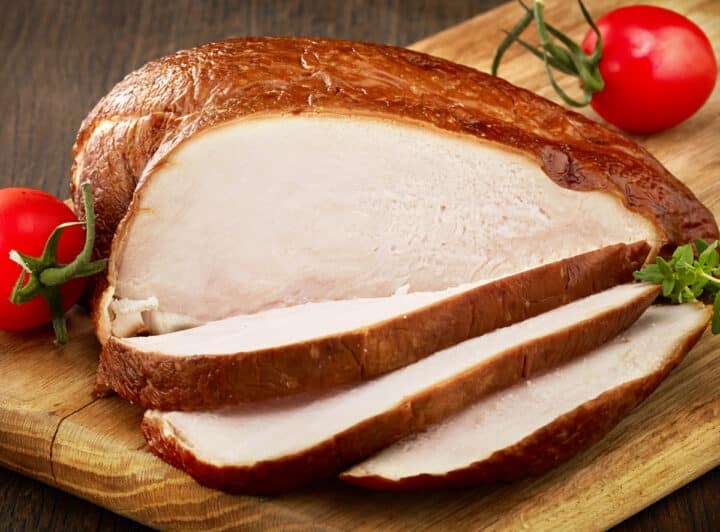 Sliced whole smoked chicken breast showing crispy skin and tender juicy meat that is no longer pink in the inside.