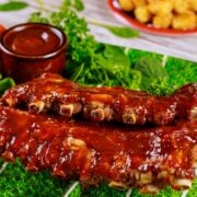 Slow cooker ribs on football themed serving tray with air fryer tater tots and extra barbecue sauce