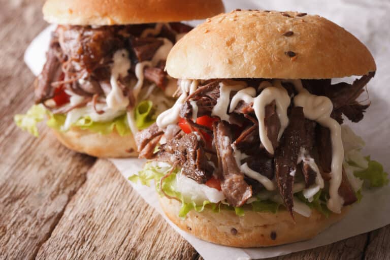 smoked chuck roast pulled and served on a bun. two sandwiches are drizzled with horseradish cream sauce.