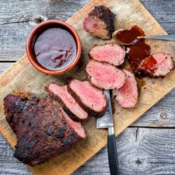 top down view of sliced smoked tri tip on a cutting board with bbq sauce on the side