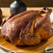 Smoked whole chicken recipe on wooden board ready to be carved.