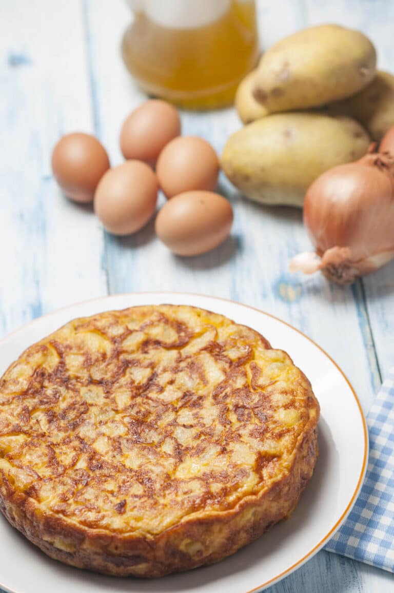 Spanish Omelet after cooking alongside ingredients for the omelete; potatoes, eggs, onions, and oil.
