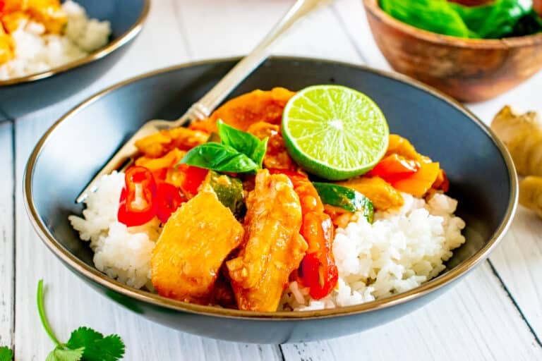 Landscape view of Thai red curry chicken on a bed of rice garnished with lime and Thai basil leaves.