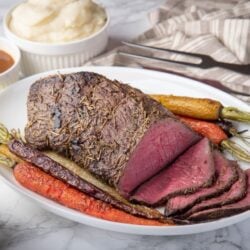 Top round roast carved on white serving platter with roasted carrots alongside ready to serve.